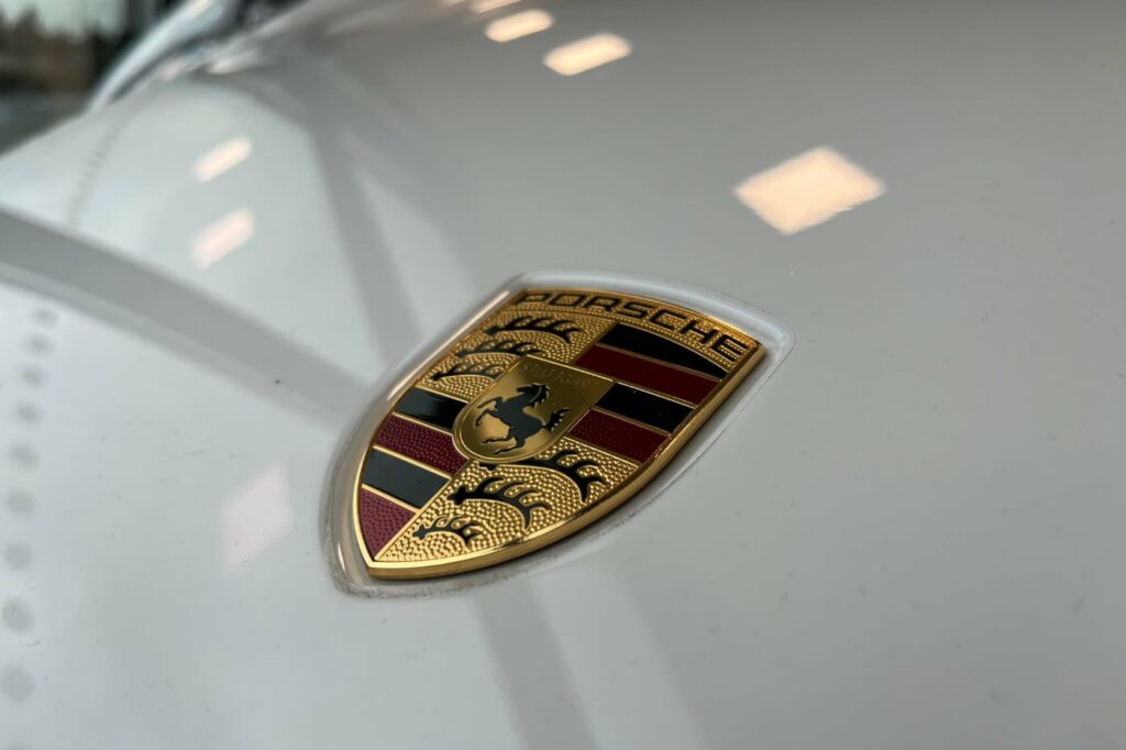 Närbild på porsche-logotyp på bilen som står parkerad i en bilhall